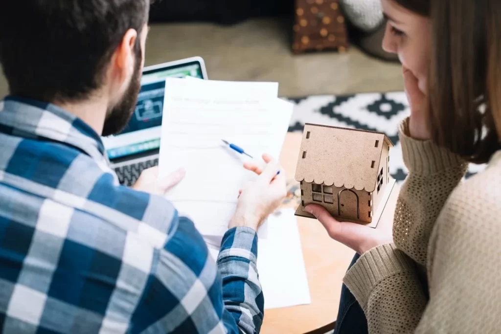 A couple in Malaysia reviews documents and holds a model house, discussing estate planning and property inheritance.