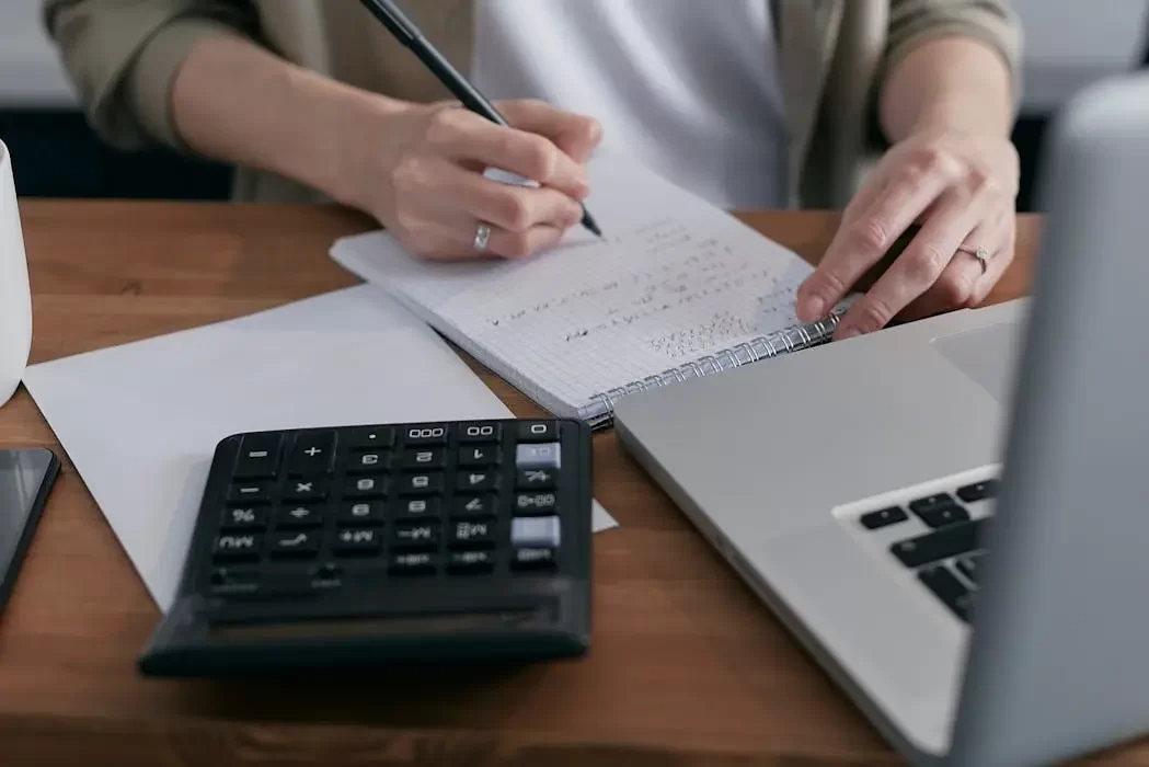 A person using a calculator and notebook to assess asset value, representing the financial planning required to balance a living trust and a will in a comprehensive estate plan.