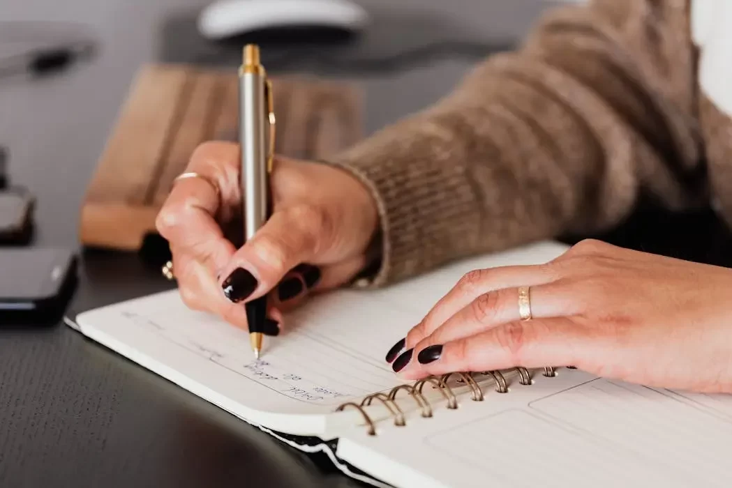 Close-up of a person writing a checklist in a notebook, representing the process of listing assets and beneficiaries for a malaysian will.