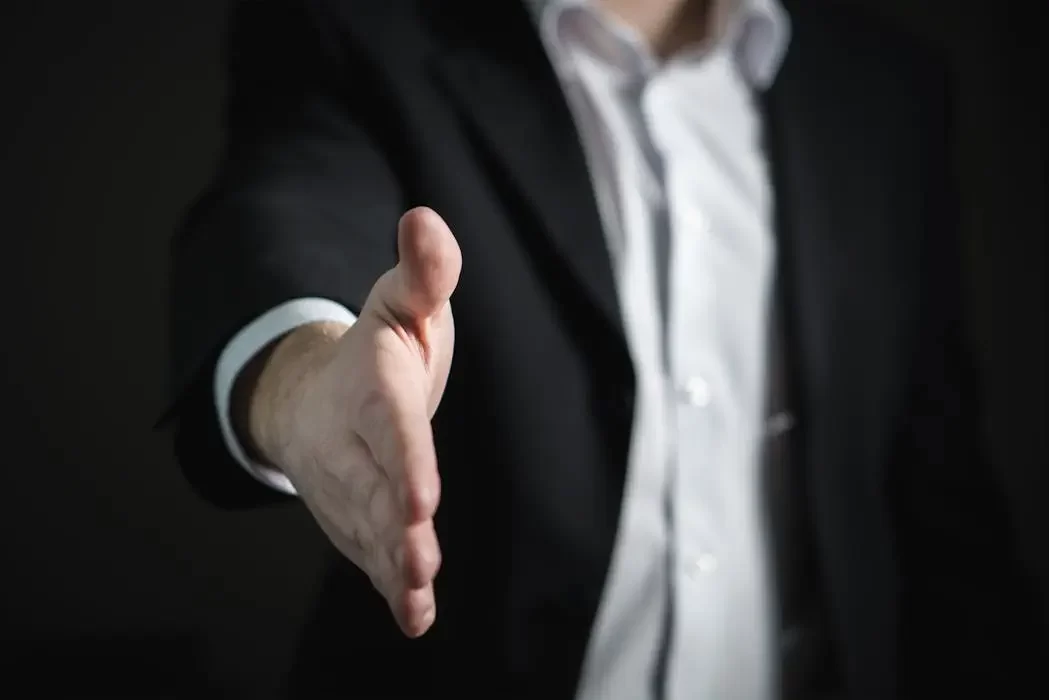 A professional lawyer in a suit extending a handshake, symbolizing the reliability and accountability of hiring a legal expert for will writing versus an unregulated individual.