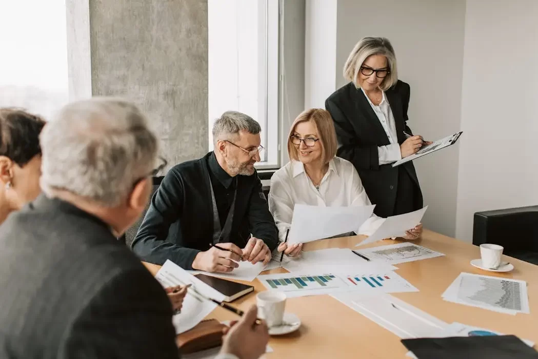A senior couple discussing estate planning steps with professional trust advisors at a meeting table, reviewing documents to set up a trust in malaysia.