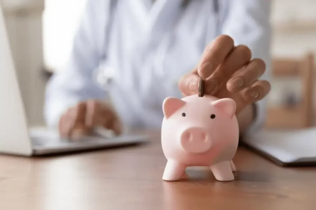 A healthcare professional inserting a coin into a piggy bank, symbolizing how a living trust allows access to funds for medical care if you become incapacitated.