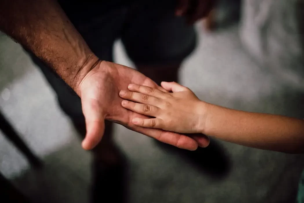 A close-up of an adult hand gently holding a child's hand, symbolizing the protection and security a trust provides for future generations.