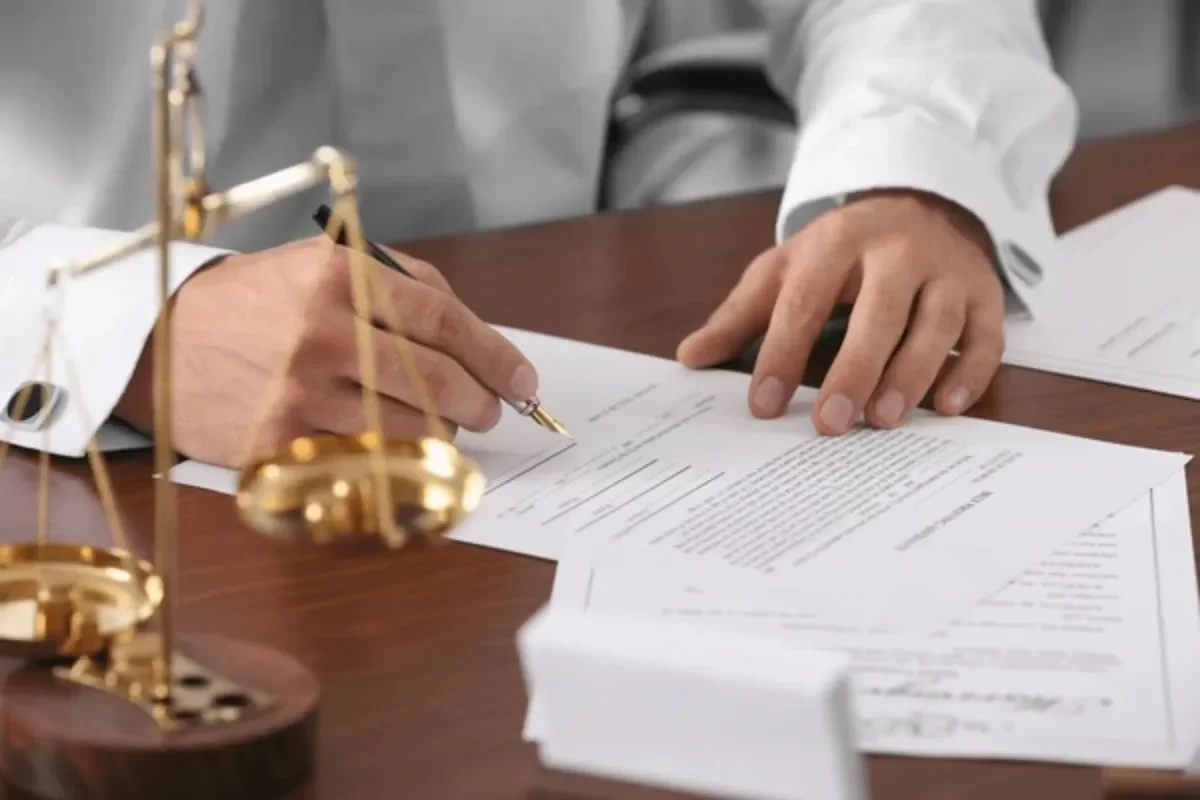 A close-up of hands signing a formal will document with a fountain pen, next to a brass scale of justice, symbolizing the legal importance of following proper will writing tips.