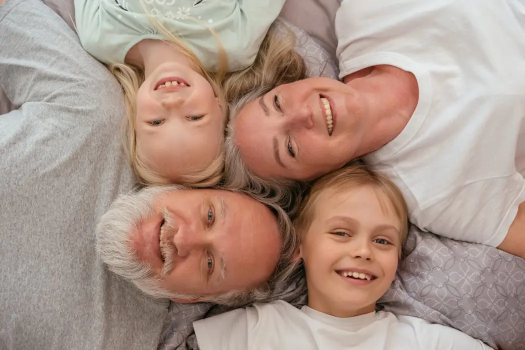 An older couple and two young children lying closely together on a bed and smiling, representing a happy blended family that requires careful estate planning in malaysia.