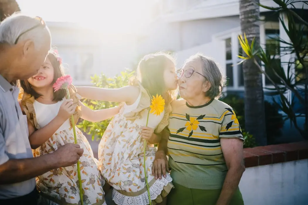 A young girl kissing an older woman on the cheek while holding flowers, representing the loving bonds in a blended family that should be protected by a family trust or will.