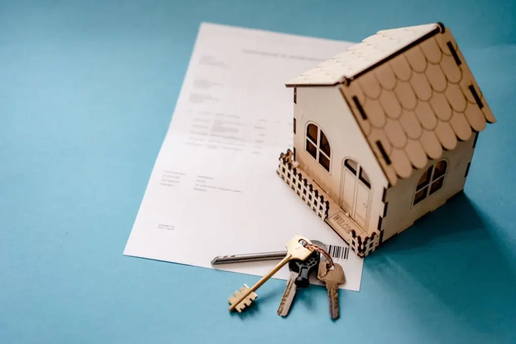 A wooden model house sitting on a legal document next to a set of keys, representing property inheritance, title transfer, and estate administration in malaysia.